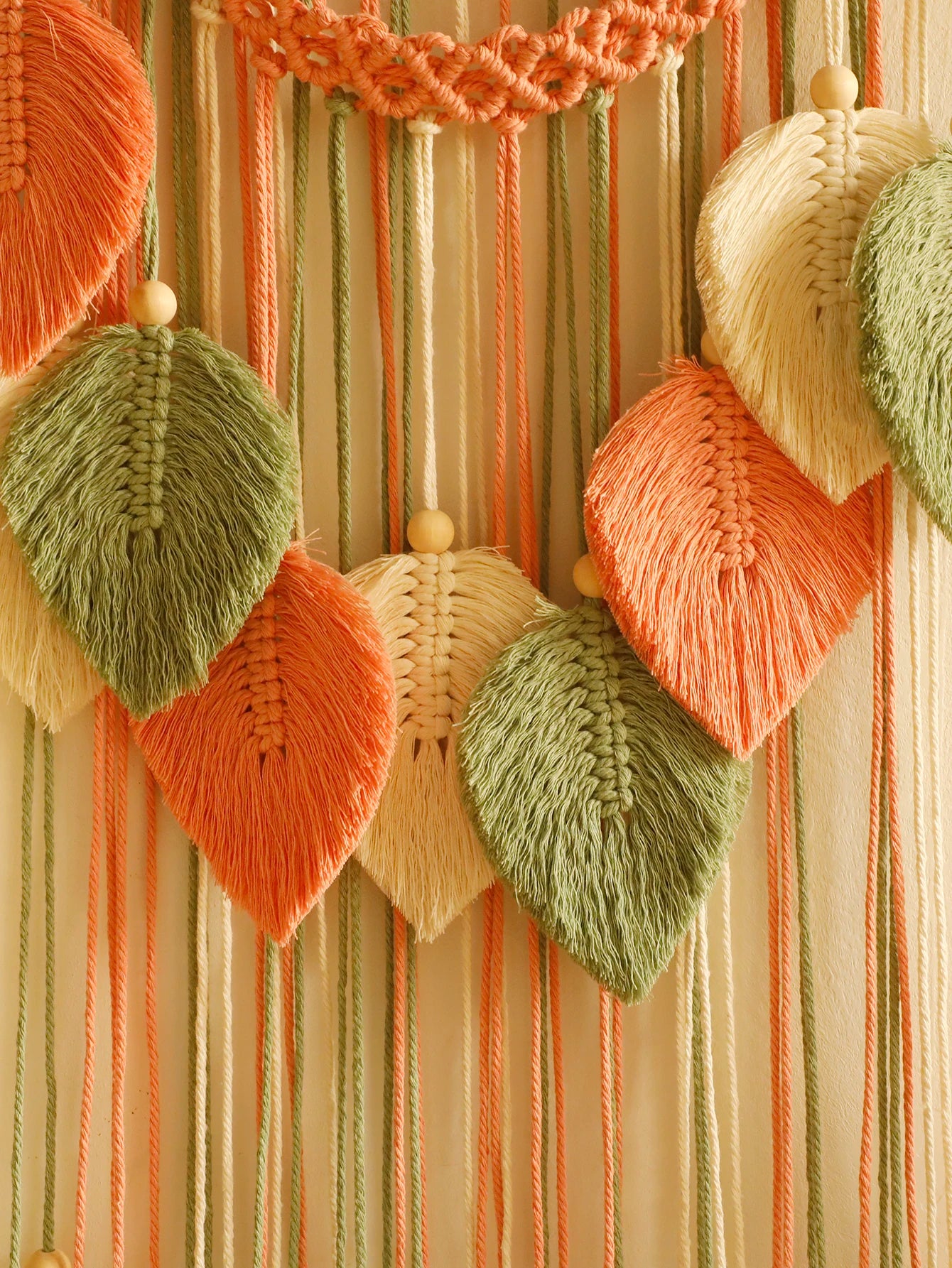 Decorative wall hanging with knitted leaf shapes in green, orange, and beige on a striped background.