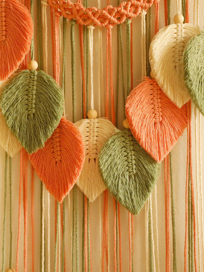 Decorative wall hanging with knitted leaf shapes in green, orange, and beige on a striped background.