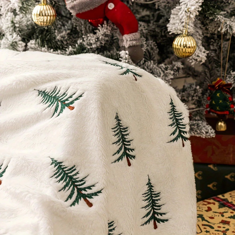 White blanket with green tree patterns in front of a decorated Christmas tree.