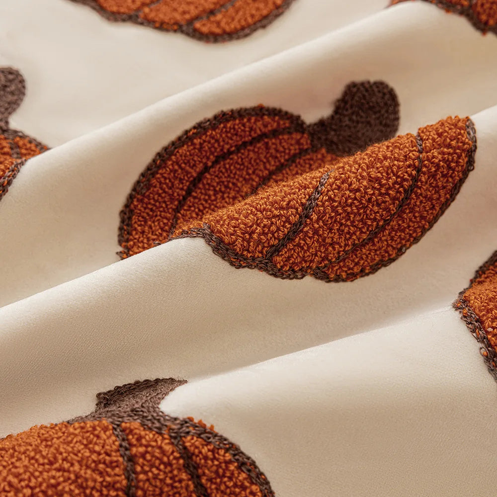 Close-up of textured brown leaves on a beige fabric surface Autumn velvet embroidered pumpkin pillow cover, Nordic-style decorative cushion for sofa, bed, and fall boho home decor