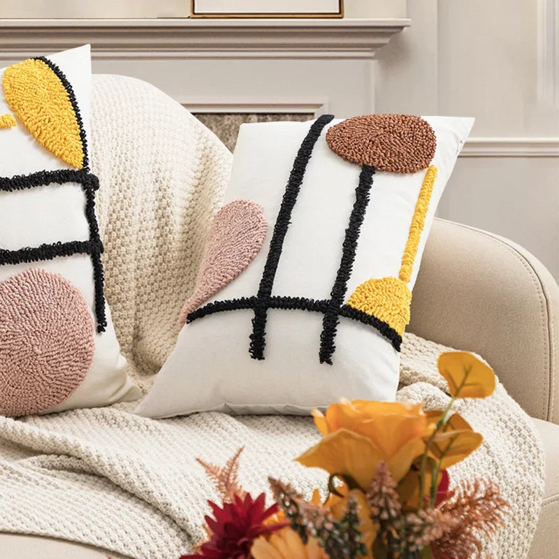 Decorative pillows with abstract patterns on a couch, accompanied by flowers. Nordic blue tufted cushion cover with geometric stripe and grid crochet pattern, tassel pillow cover for sofa, bed, and boho home decor