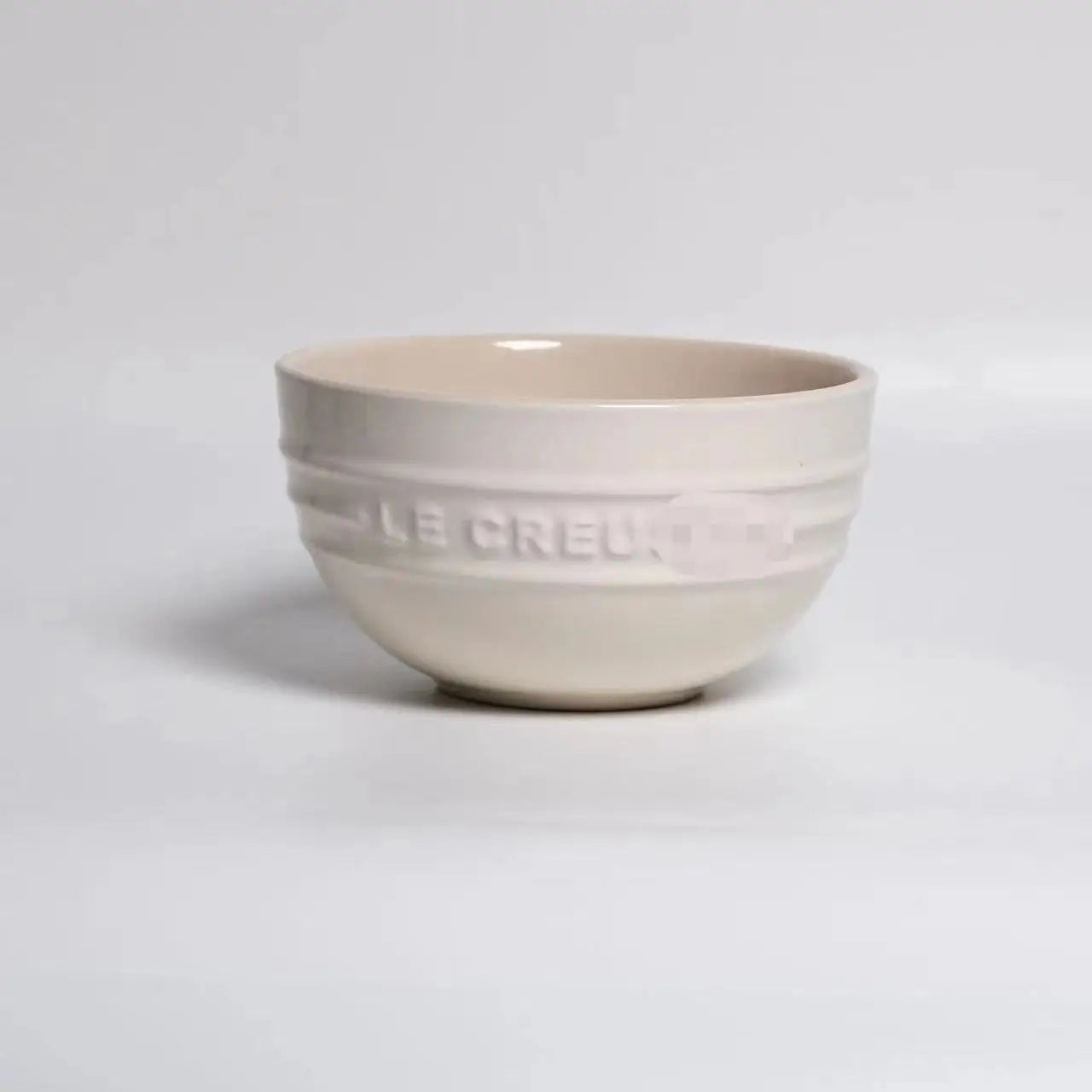 Beige ceramic bowl with 'Le Creuset' branding on a light gray background Gradient ceramic rice bowl in bright colors, bone china soup and noodle bowl, dessert and pudding kitchen tableware for boho home dining