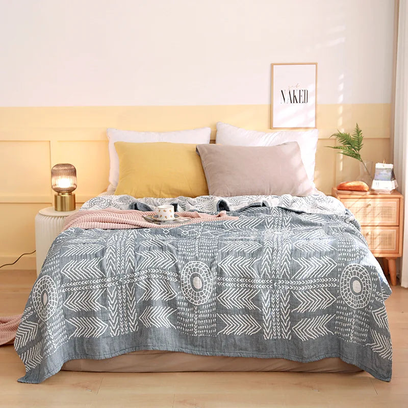 Bed with a gray patterned blanket and colorful pillows in a bedroom setting. Boho Lightweight microfiber summer blanket for bed or sofa, cooling breathable throw for home, dorm, or office naps with geometric jacquard pattern.