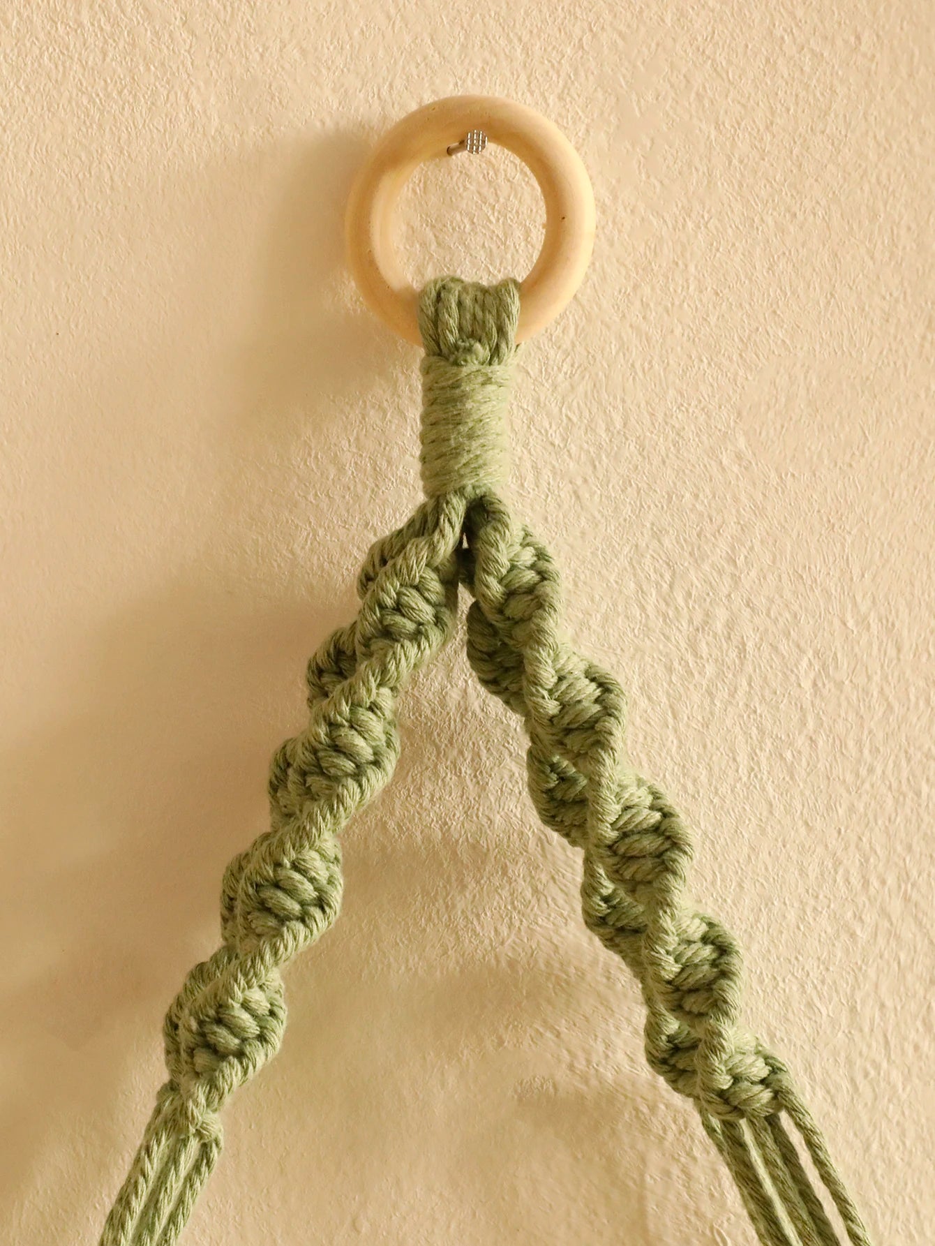Green macrame shelf with wooden ring on a beige wall