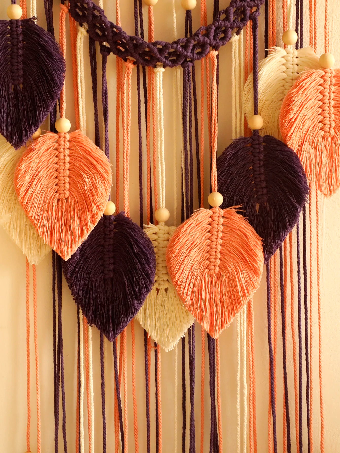 Macrame wall hanging with leaf-shaped decorations on a striped background