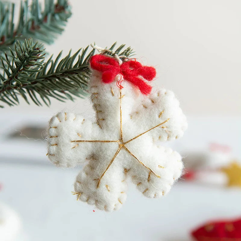 White felt snowflake ornament with gold accents and a red ribbon on a blurred Christmas tree branch background.
