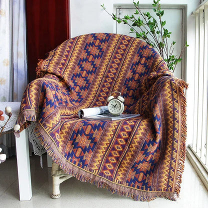 Patterned blanket draped over a chair with a clock and rolled-up paper on a white floor. Mediterranean style woven cotton throw blanket boho home decor