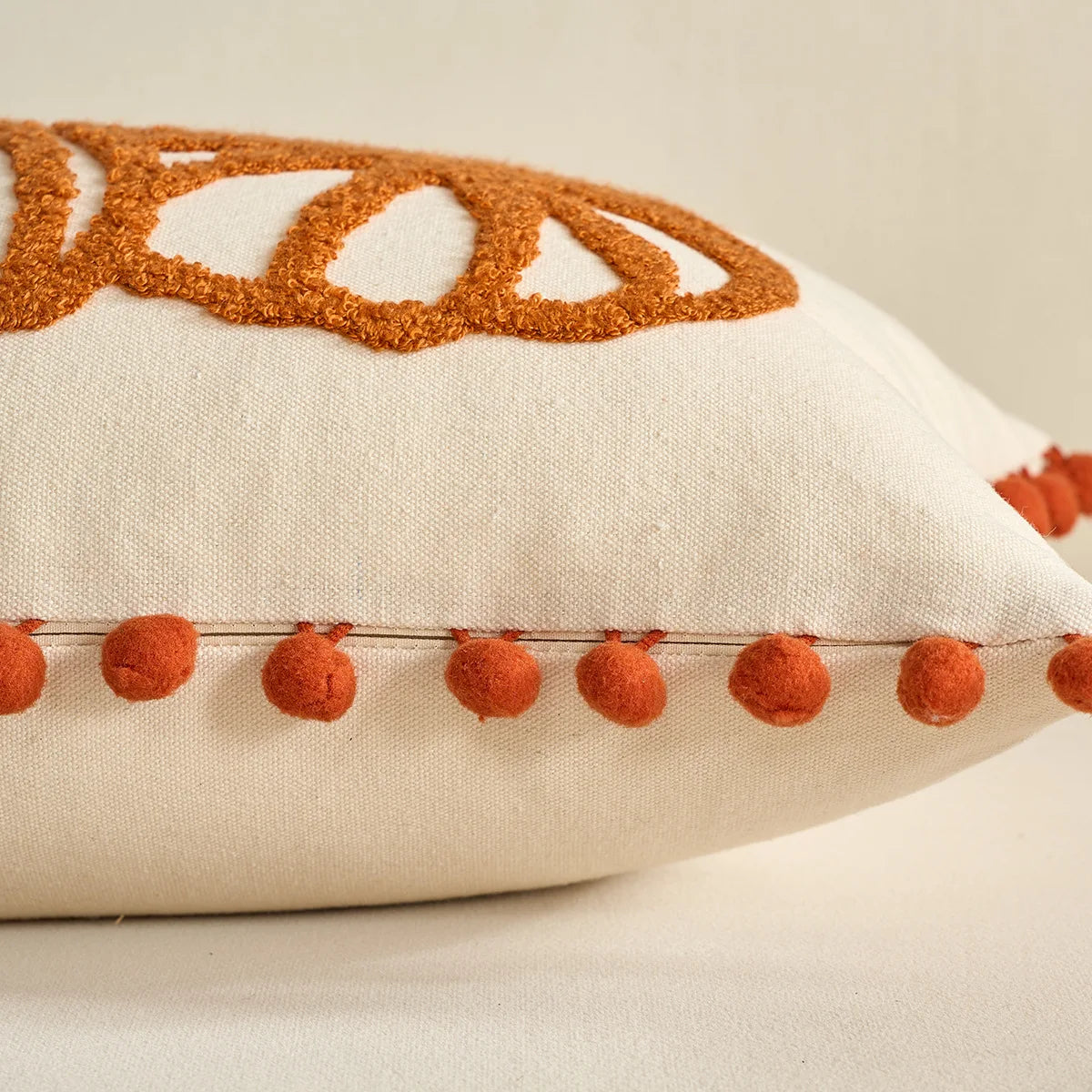 Decorative pillow with brown embroidered design and red pom-poms on a beige background. Festive autumn pumpkin cushion case for sofa or bed