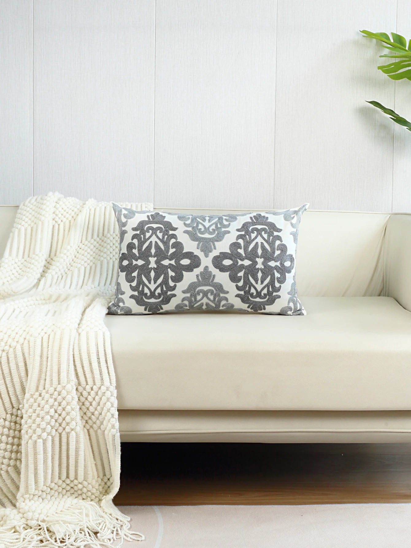 Decorative pillow with a gray pattern on a white couch with a white blanket.