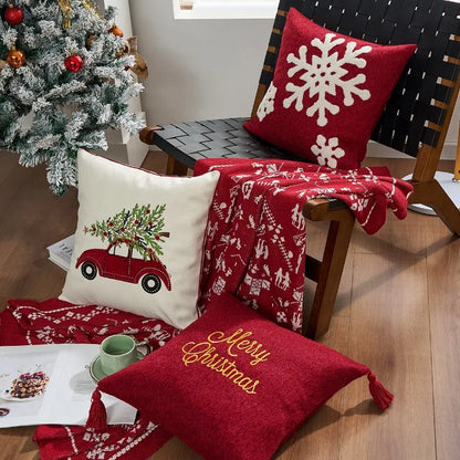 Decorative pillows with Christmas designs on a chair next to a tree. Christmas gold letter embroidered pillow cover with “Holly Jolly” and snowflake design, soft red and white chenille cushion case for sofa or living room holiday décor.