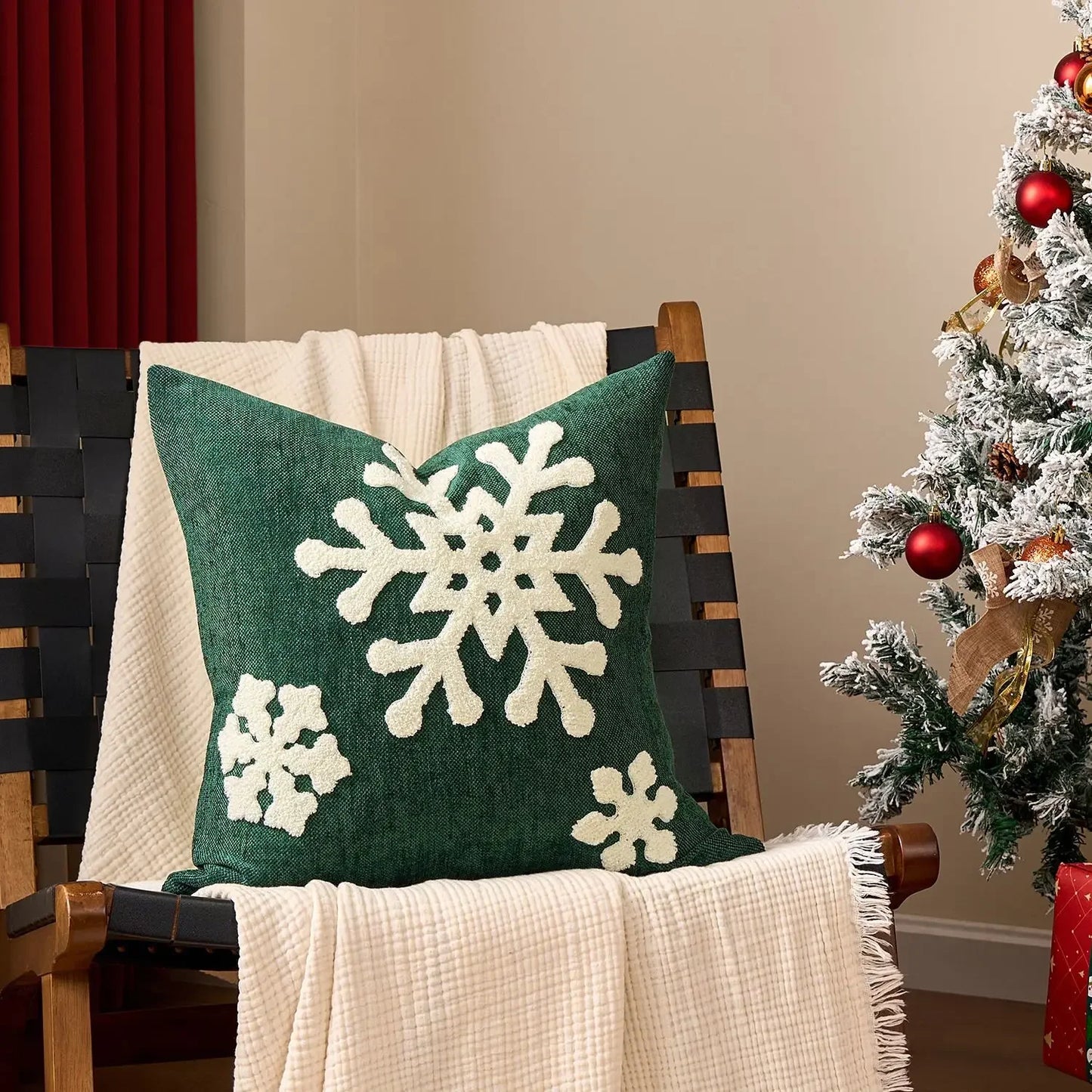 Green pillow with snowflake patterns on a chair next to a decorated Christmas tree. Embroidered Merry Christmas pillow cover with snowflake design – festive red and white holiday cushion for sofa or bedroom décor.