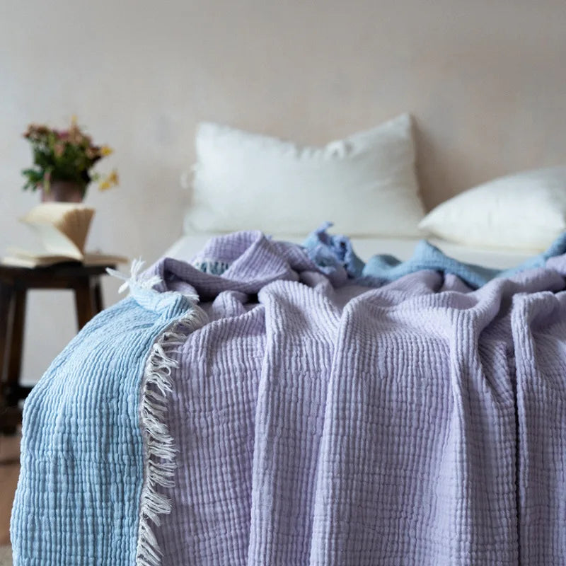 Bed with layered textured blankets and pillows in a cozy room. Maillard cotton gauze blanket with tassels, four-layer muslin throw for sofa, bed, and boho home decor