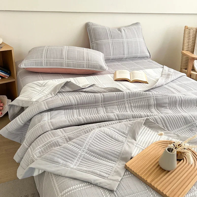Bed with gray textured bedding, pillows, and a book on a wooden nightstand. Boho breathable lightweight summer spring fall blanket quilt bedspread 