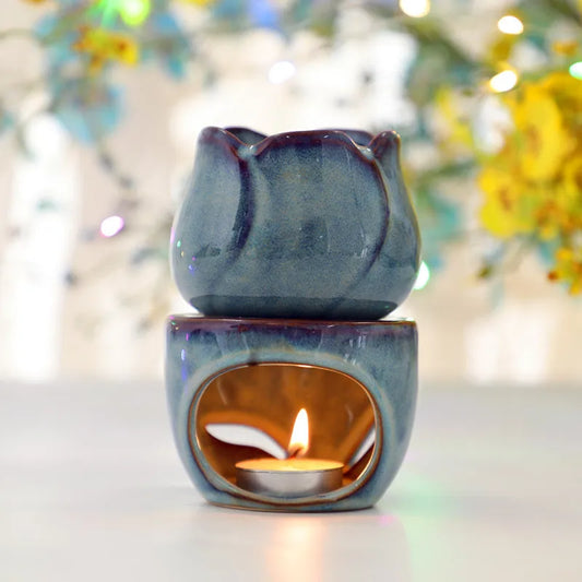 Blue ceramic oil burner with a lit candle inside, set against a blurred floral background. tulip ceramic essential oil incense burner, candle-powered aroma diffuser for home fragrance and calming boho home décor