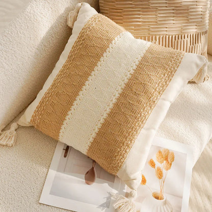 Textured pillow with tassels on a soft surface next to a woven basket.
