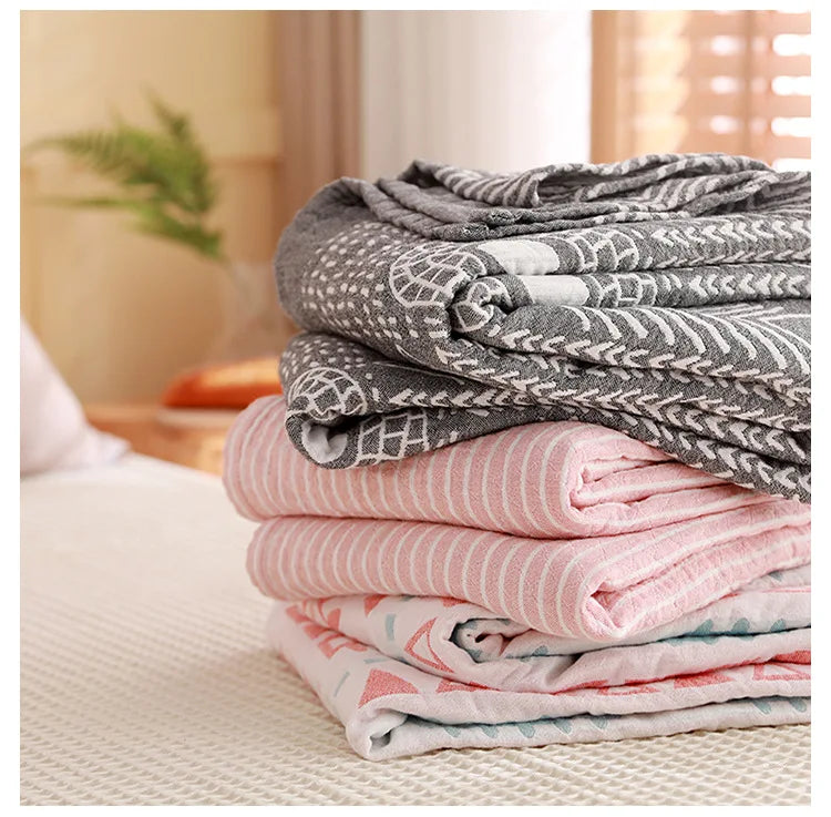 Stack of folded blankets in gray, pink, and white patterns on a bed. Boho Lightweight microfiber summer blanket for bed or sofa, cooling breathable throw for home, dorm, or office naps with geometric jacquard pattern.