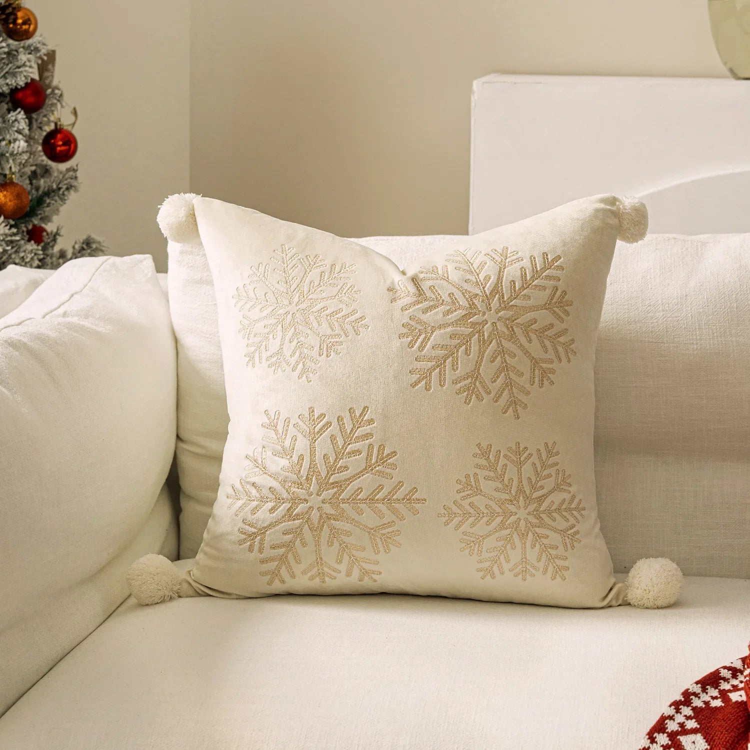 Decorative pillow with snowflake patterns on a beige couch next to a Christmas tree. Embroidered Merry Christmas pillow cover with snowflake design – festive red and white holiday cushion for sofa or bedroom décor.