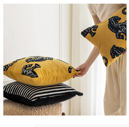 Person holding a yellow pillow with black patterns next to two other pillows on a surface. Modern minimalist embroidered pillow cover for living room decor.