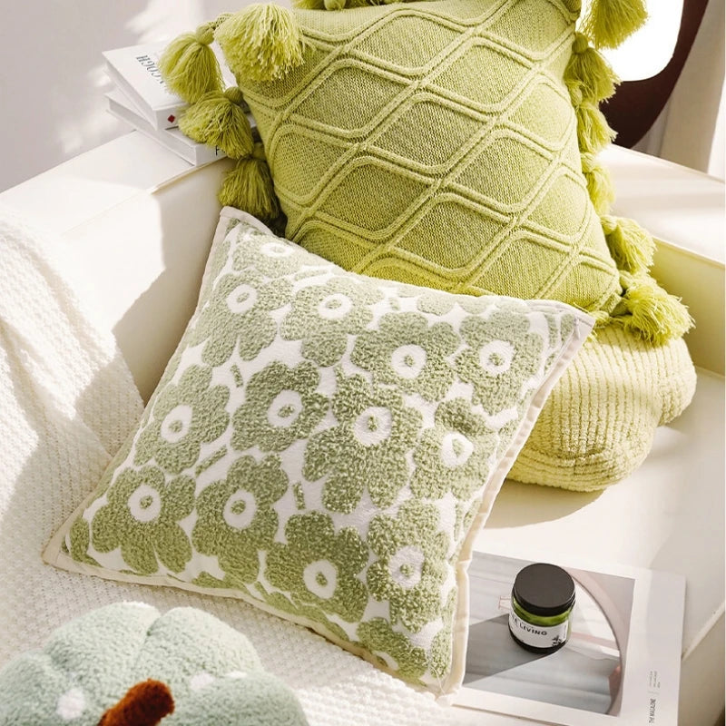 Green patterned cushions on a sofa with a small jar and book.