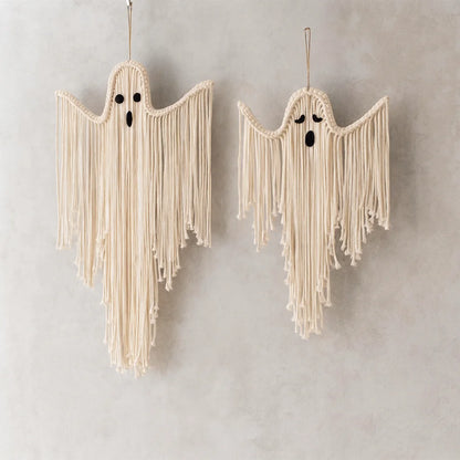 Two cream macrame ghost wall hangings with black embroidered eyes and mouths, hanging against a textured light gray wall from My Boho Home