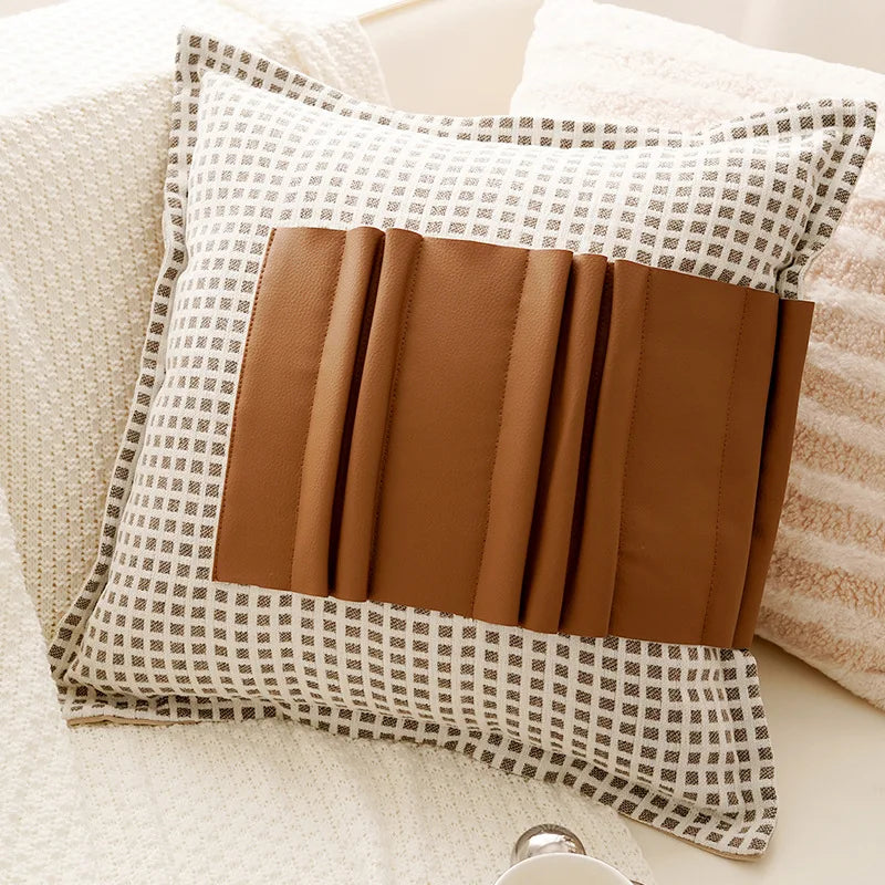 Decorative pillow with plaid pattern and brown leather accents on a beige sofa.
