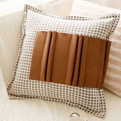 Decorative pillow with plaid pattern and brown leather accents on a beige sofa.