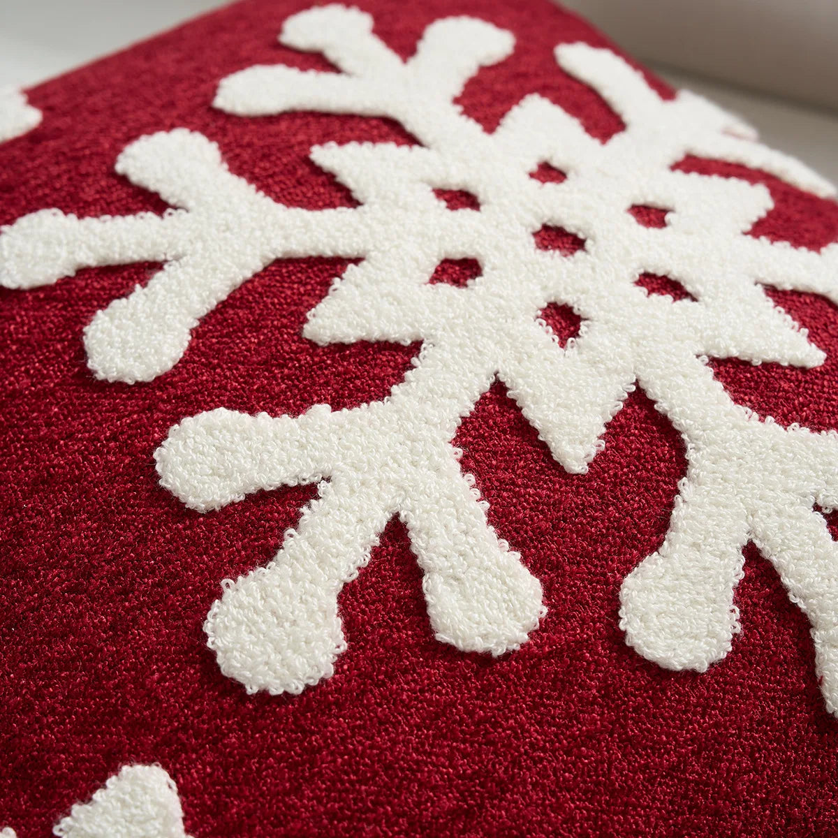 Red fabric with white snowflake patterns. Embroidered Merry Christmas pillow cover with snowflake design – festive red and white holiday cushion for sofa or bedroom décor.