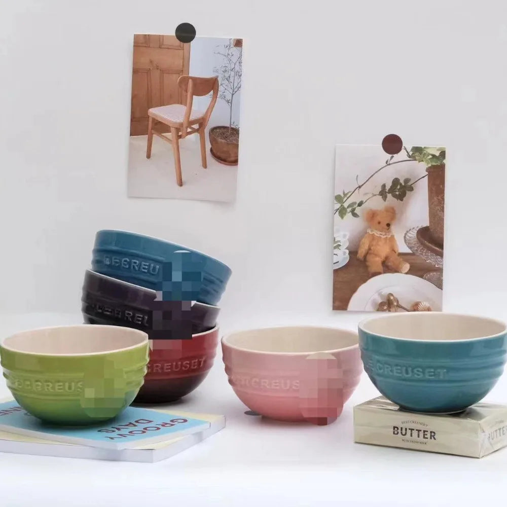 Set of colorful ceramic bowls with 'LE CREUSET' branding on a white surface. Gradient ceramic rice bowl in bright colors, bone china soup and noodle bowl, dessert and pudding kitchen tableware for boho home dining