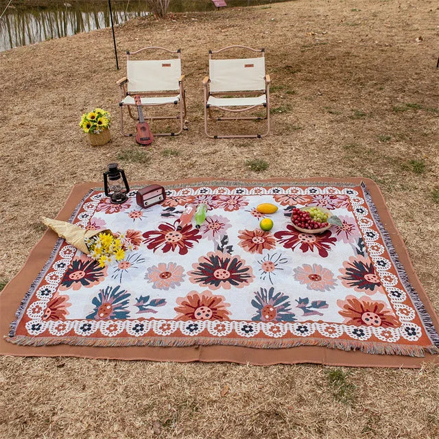 Floral-patterned picnic blanket with chairs and picnic items on a grassy field. Mediterranean style woven cotton throw blanket boho home decor