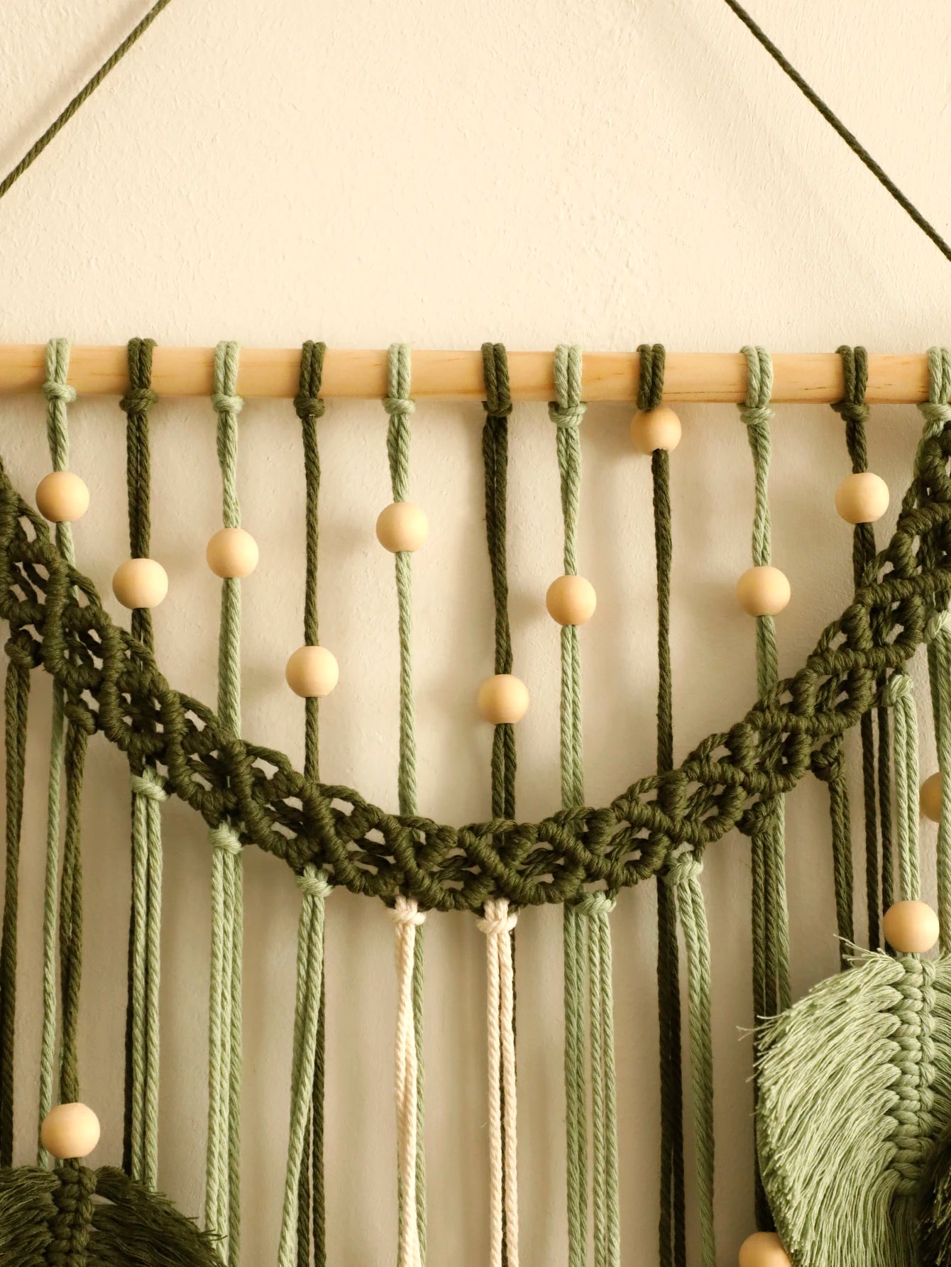 Macrame wall hanging with green ropes and wooden beads on a neutral background