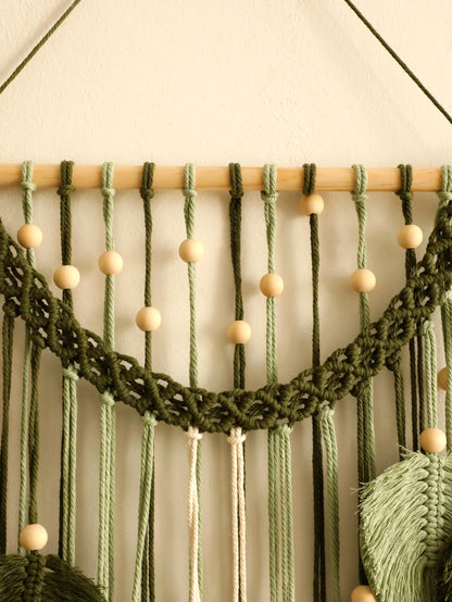 Macrame wall hanging with green ropes and wooden beads on a neutral background