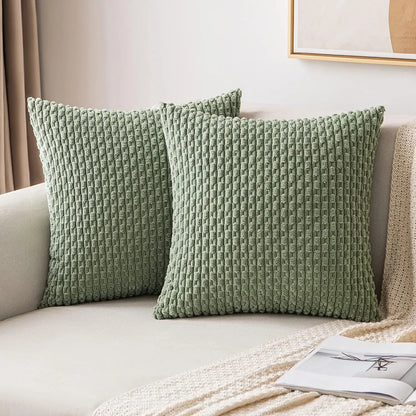 Two sage green textured pillows on a beige sofa with a neutral background