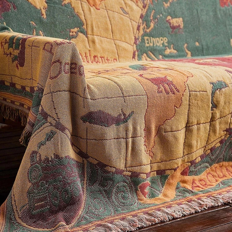 Map-themed quilt draped over a couch with world map design. Travel-inspired cotton plaid bed cover and decorative boho blanket