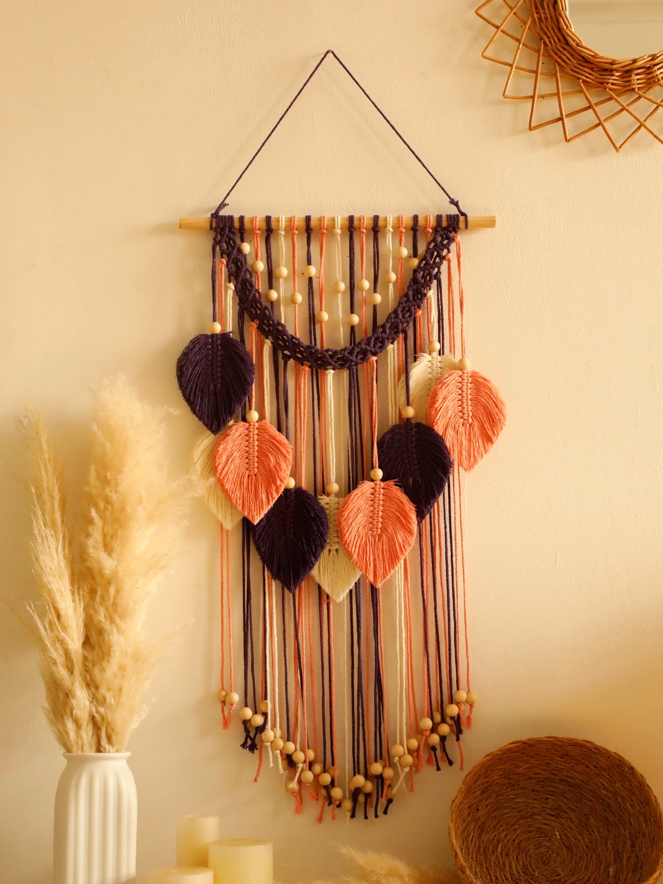 Decorative leaf macrame wall hanging with ribbons and beads on a neutral wall.