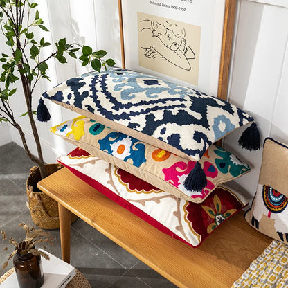Colorful patterned cushions on a wooden bench with a plant and artwork in the background. Bohemian embroidered throw pillow cover with geometric design, cotton-blend cushion for sofa, bed, or modern home decor.