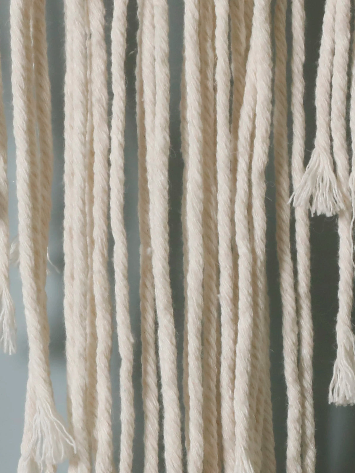 Close-up of cream-colored cotton fringe tassels hanging vertically against a muted gray background from My Boho Home