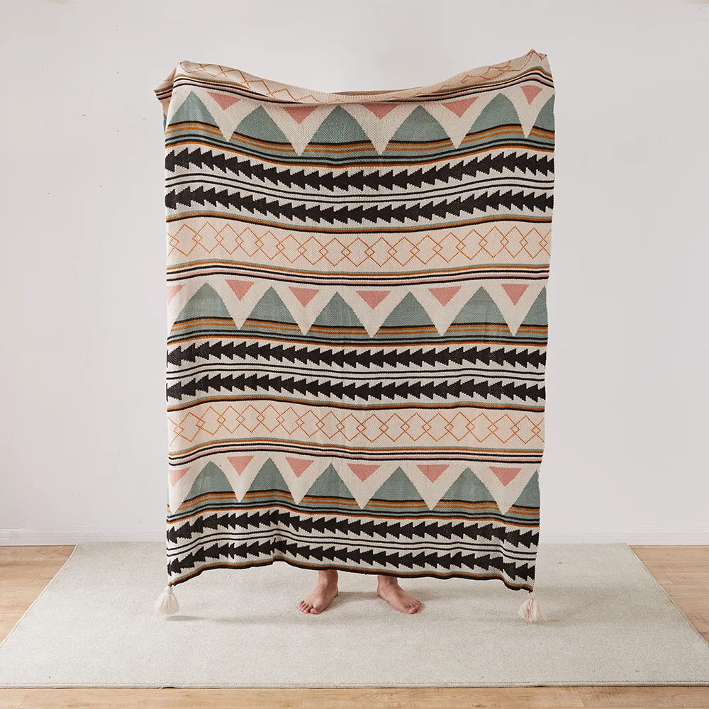 Patterned Bohemian blanket draped over a person on a wooden floor with a white wall background