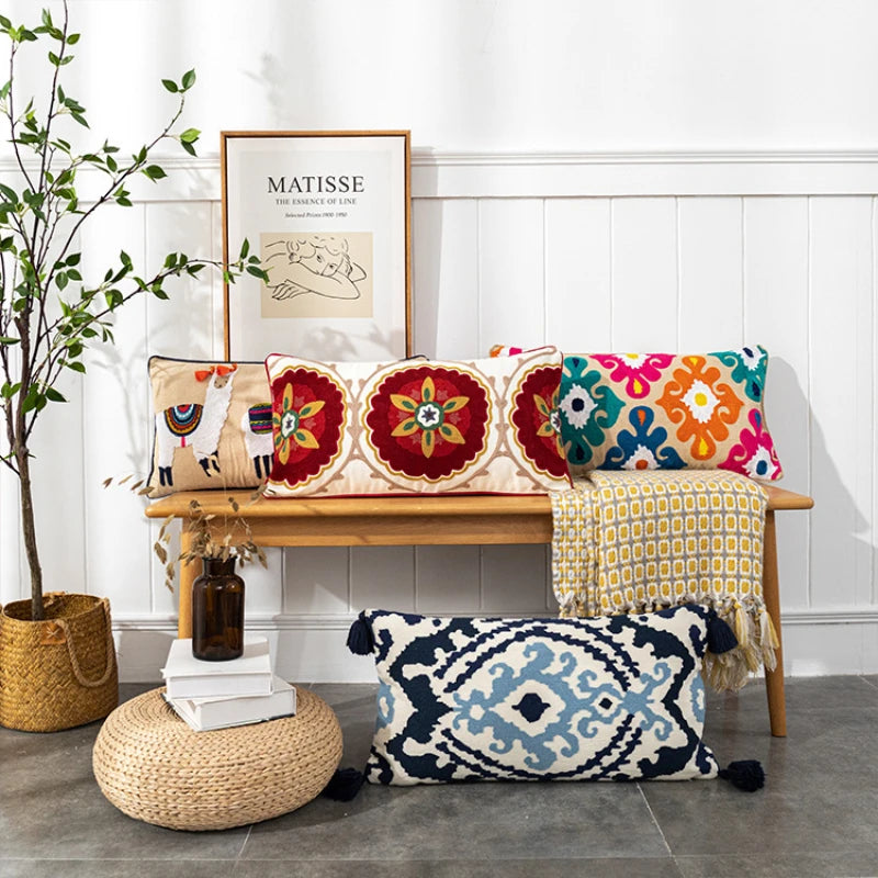 Decorative pillows on a bench with a plant and framed art in the background.Bohemian embroidered throw pillow cover with geometric design, cotton-blend cushion for sofa, bed, or modern home decor.