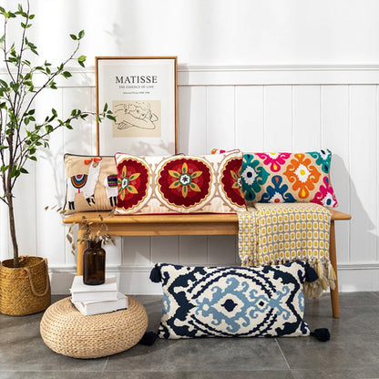 Decorative pillows on a bench with a plant and framed art in the background.Bohemian embroidered throw pillow cover with geometric design, cotton-blend cushion for sofa, bed, or modern home decor.