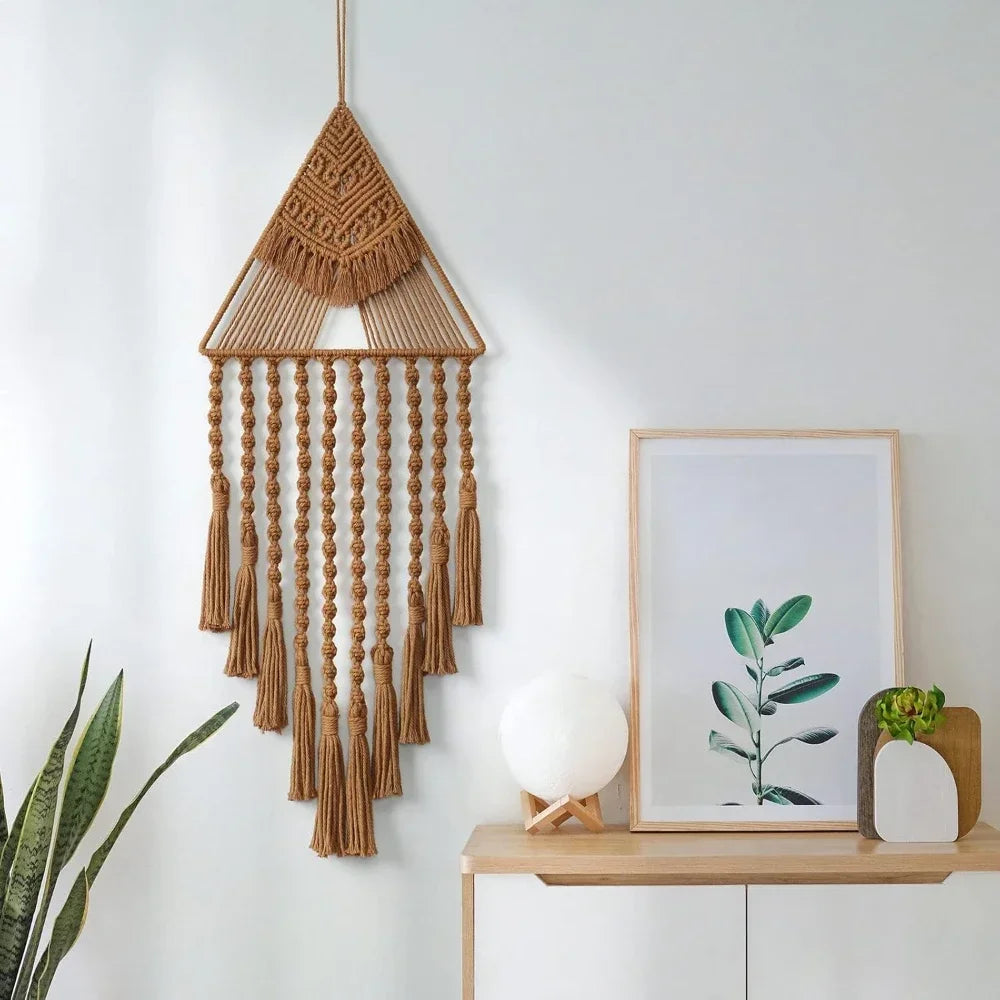 Macrame wall hanging on a white wall with a framed plant print and decorative items. boho home decor, macrame wall hanging, triangle dream catcher, woven tapestry, handmade cotton wall decor, tassel wall hanging, bedroom door decor, housewarming gift, rustic bohemian art, boho apartment wall decor, neutral textile art