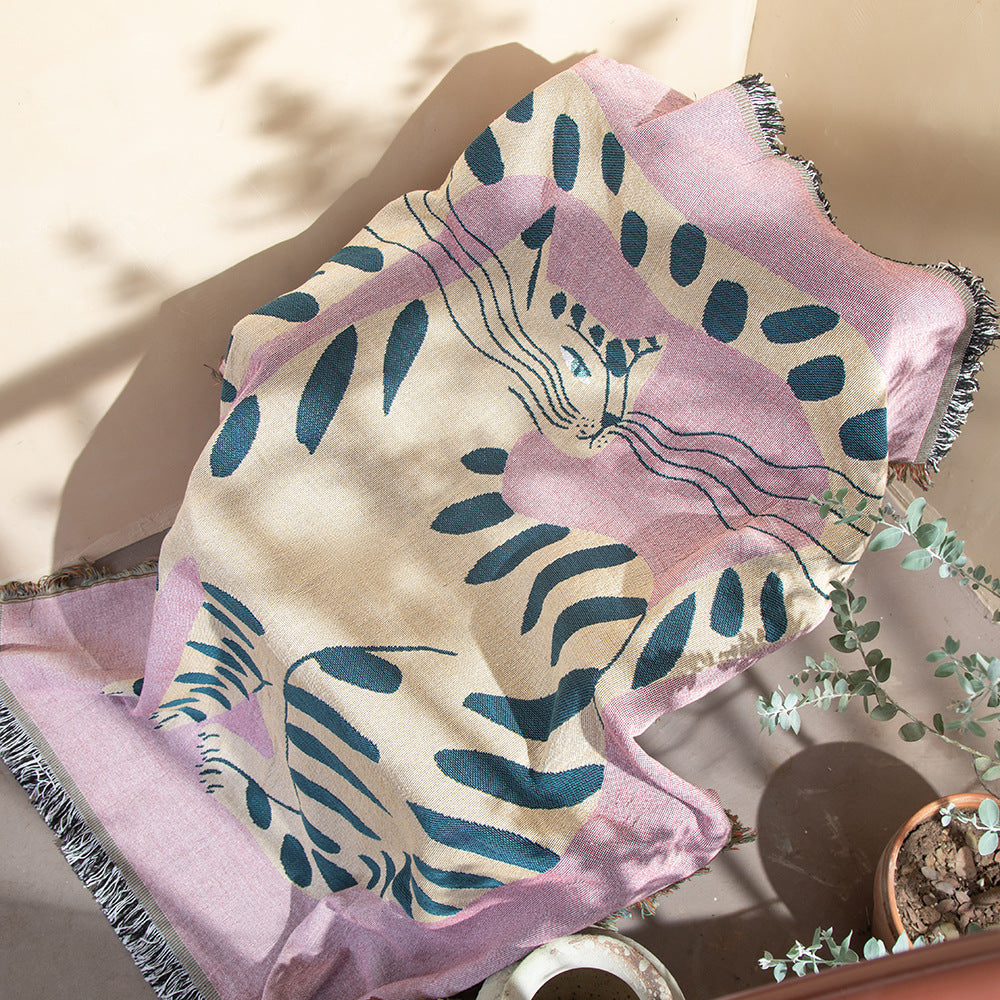 Pink and blue patterned towel on a surface with a plant in the background. boho woven cotton tapestry with pink girl cat design