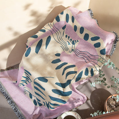 Pink and blue patterned towel on a surface with a plant in the background. boho woven cotton tapestry with pink girl cat design