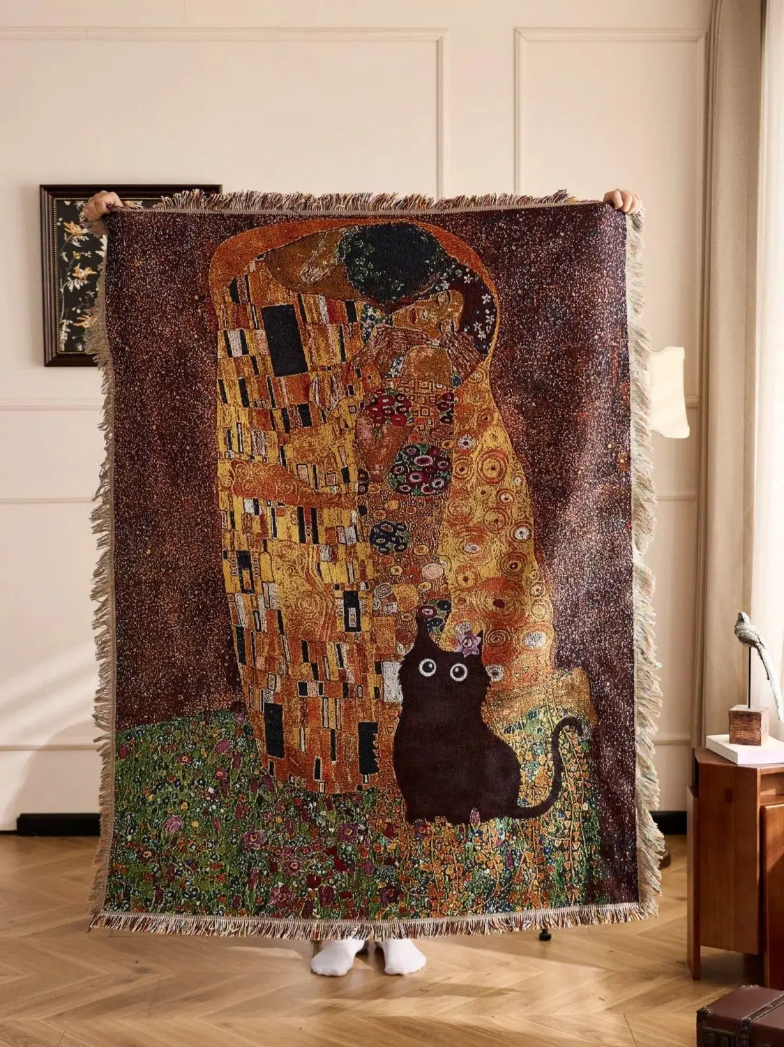 Blanket with 'The Kiss' design by Gustav Klimt featuring a cat, held up indoors. Cat woven throw blanket for boho sofa and home decor