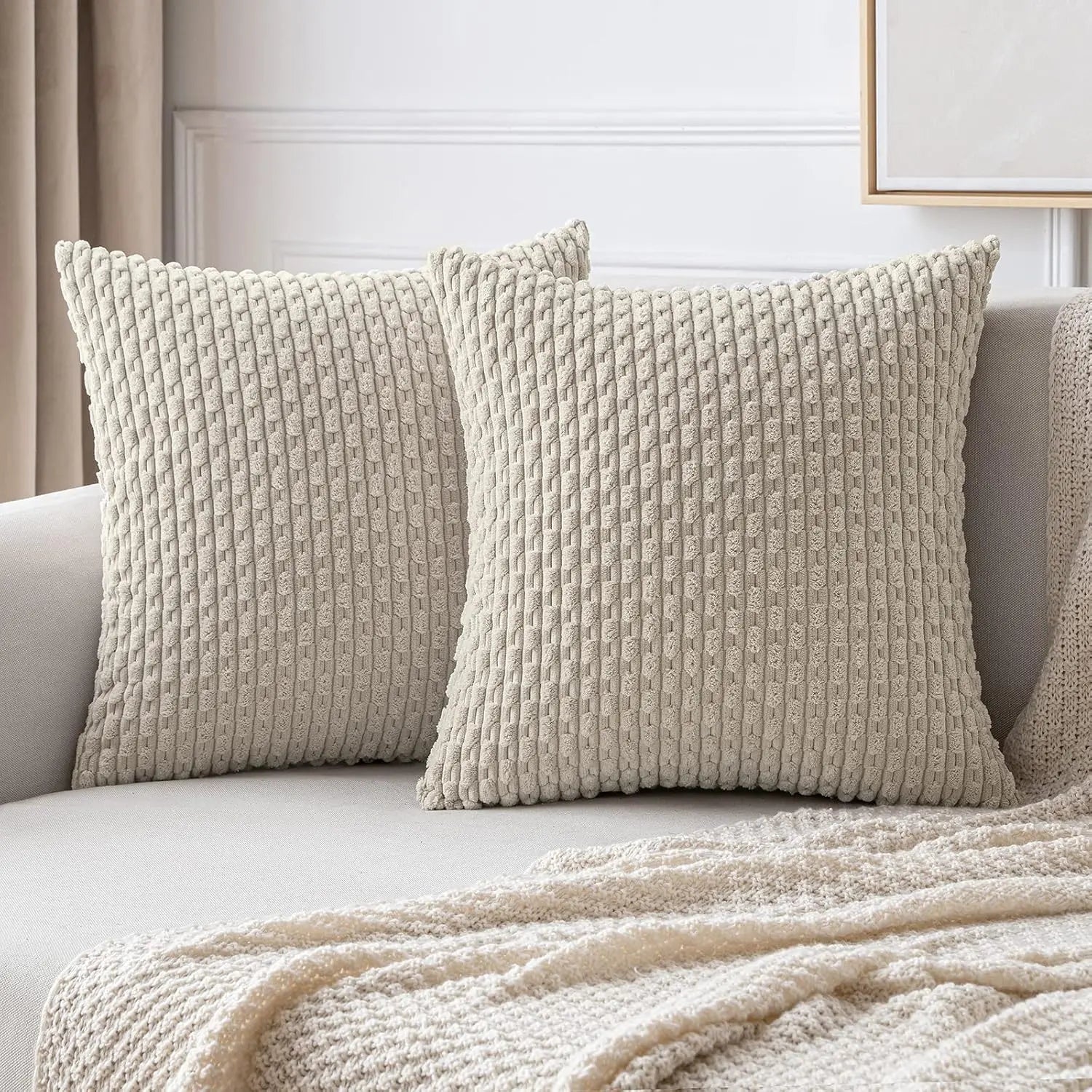 Two textured beige pillows on a sofa with a neutral background
