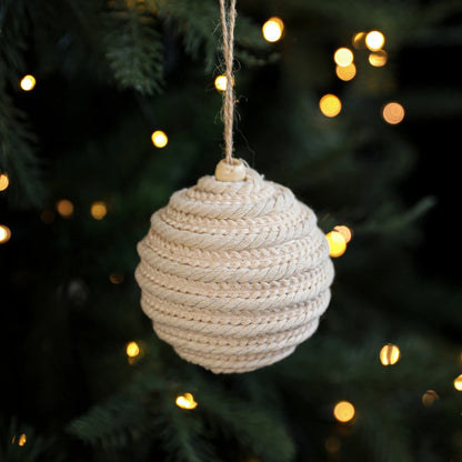 Woven beige ornament hanging on a Christmas tree with blurred lights in the background