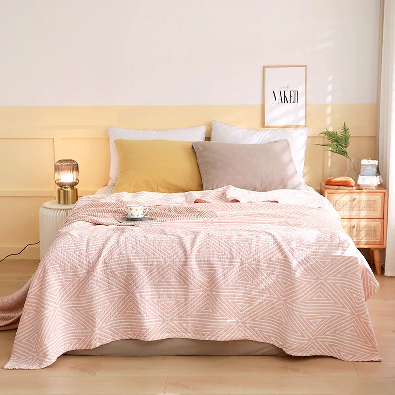 Bedroom with a bed covered in pink bedding, white pillows, and a yellow headboard. Boho Lightweight microfiber summer blanket for bed or sofa, cooling breathable throw for home, dorm, or office naps with geometric jacquard pattern.