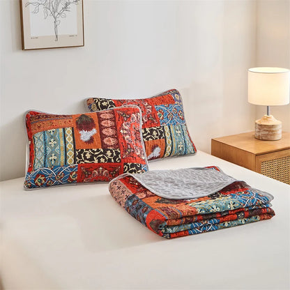 Colorful patchwork quilt and pillows on a bed with a lamp and artwork in the background. Lightweight boho quilted bedspread set with pillow shams, soft all-season coverlet for queen, king, full, or twin beds in modern cloud pattern design.