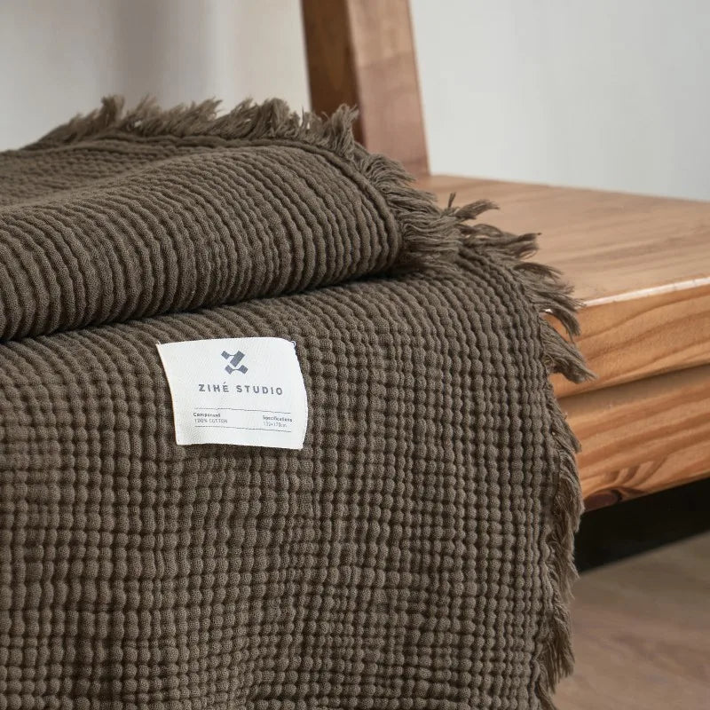Brown textured blanket with a label on a wooden surface Maillard cotton gauze blanket with tassels, four-layer muslin throw for sofa, bed, and boho home decor