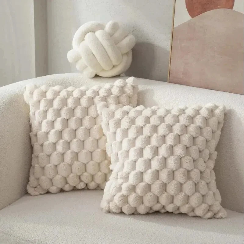 Textured white pillows on a light-colored sofa with a decorative knot pillow in the background.