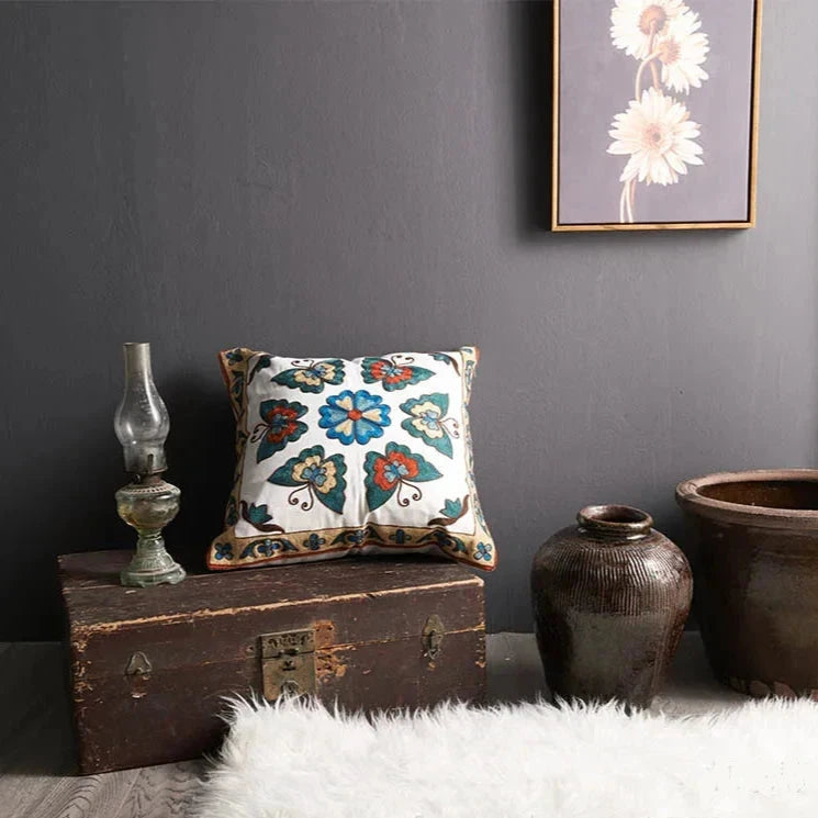 Decorative pillow with floral pattern on a wooden chest against a gray wall. floral embroidery on linen cotton cushion cover – boho home decor accent